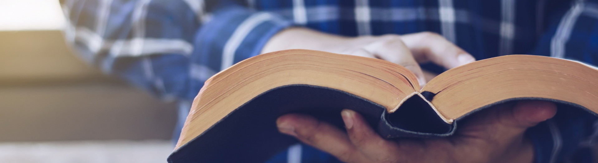 Close up of Young christian man standing at concrete wall while read bible with window light